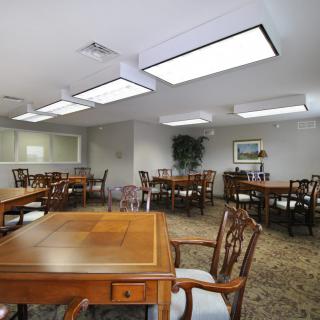 A well-lit meeting room with multiple wooden tables and chairs, suitable for gatherings or conferences.