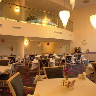 A modern restaurant dining area with empty tables set for service beneath elegant chandeliers.