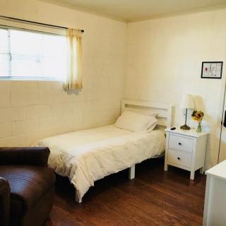 A simple and cozy bedroom with a single bed, nightstand, lamp, and a window letting in natural light.