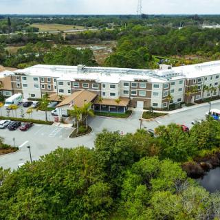 Aerial view of a hotel surrounded by trees with a parking lot in front.
