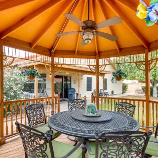 A cozy backyard gazebo with ornate metal furniture and a ceiling fan, surrounded by a lush garden.