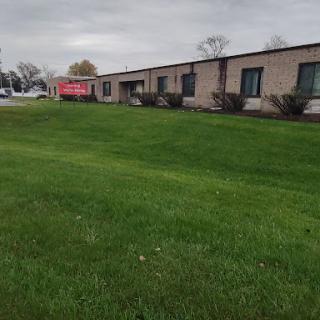 A view of a single-story building surrounded by well-maintained grass, under a cloudy sky.