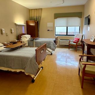 A view of a hospital patient room featuring two beds and basic furnishings.