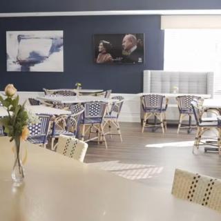 A cozy cafe interior with empty tables and chairs, decorated with flowers and artwork on the walls.