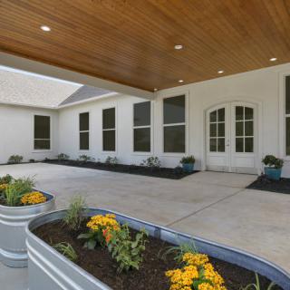 A modern building entrance featuring a wooden ceiling, large windows, and decorative planters with vibrant flowers.