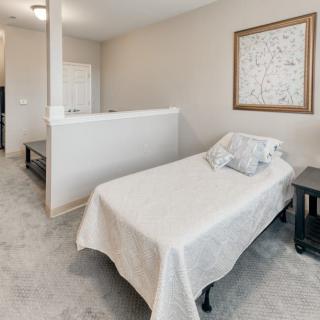 A minimalist bedroom featuring a single bed with white bedding, a nightstand, and framed artwork on the wall.