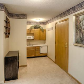 A small apartment hallway leading to a kitchen area with wooden cabinets and carpet flooring.