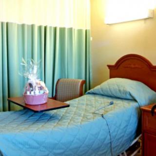 A hospital room featuring a single bed, curtain divider, and a gift basket on the table.
