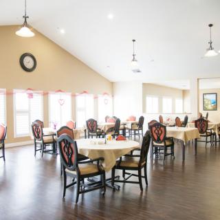 A bright and spacious dining room with multiple tables and chairs, featuring large windows for natural light.