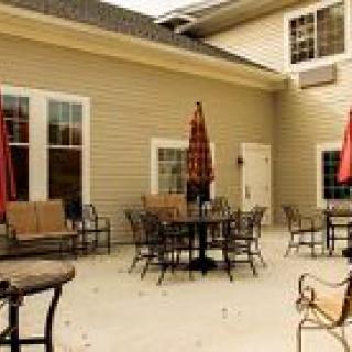 An inviting patio area with tables and chairs, shaded by red umbrellas, against a light-colored building exterior.