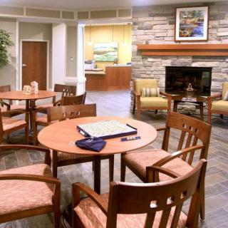 A cozy lounge with wooden tables and chairs, featuring a television and a fireplace in the background.