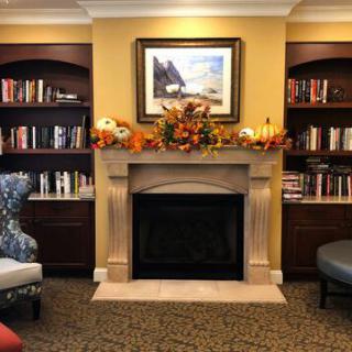 A cozy living room with a fireplace decorated for autumn, surrounded by bookshelves filled with books.