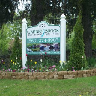 A sign for Garden Brooks Landscaping surrounded by greenery and flowers.