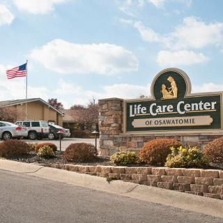 A nursing home facility with a sign, parking lot, and American flag in the background.