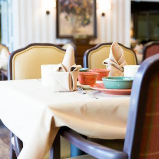 A neatly set dining table in a restaurant with plates, napkins, and chairs.