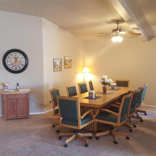 A conference room with a large meeting table surrounded by office chairs, featuring a ceiling fan and wall clock.