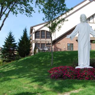 A statue stands in front of a building surrounded by trees and manicured landscaping.