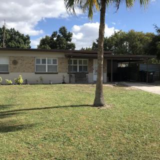 A single-story suburban house with a palm tree in the front yard under a partly cloudy sky.
