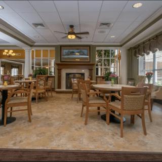 A cozy dining area with tables and chairs, featuring a central fireplace and ample natural light.