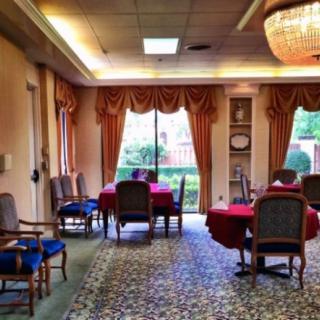 A formal dining room with elegantly set tables and chairs, featuring a chandelier and large windows with draped curtains.
