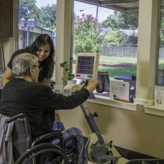 A healthcare professional assisting an elderly patient with rehabilitation exercises in a therapy room.