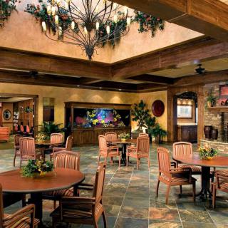 A cozy interior lounge with tables and chairs, decorated with plants and a chandelier.