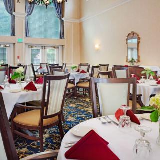 An elegant dining room with neatly set tables and chairs, featuring red napkins and floral centerpieces.