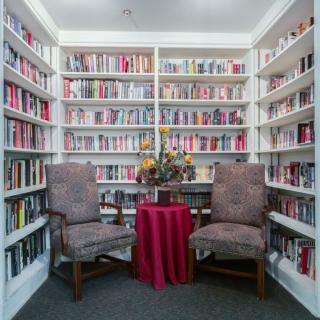 A cozy reading nook in a library with two armchairs, a small table, and shelves filled with books.
