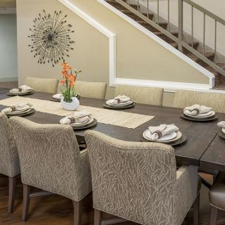 Elegant dining room with a large table set for eight, featuring modern decor and a decorative wall piece.