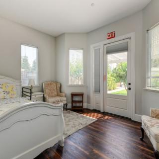 A cozy bedroom with natural light, featuring a bed, chair, and hardwood flooring.