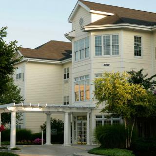 A large residential building with multiple windows and a white exterior, surrounded by trees.