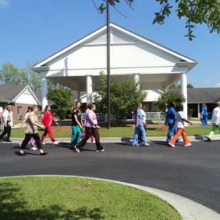 A group of people walking outdoors near a large building on a sunny day.