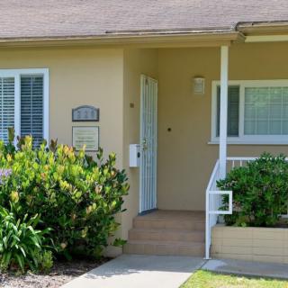 A small house entrance with a porch, surrounded by plants.