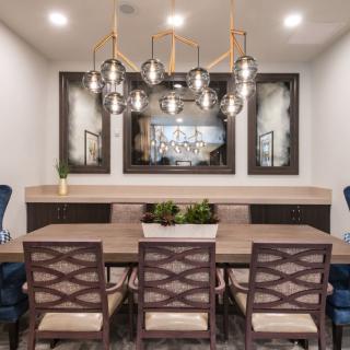 A modern dining room featuring a stylish chandelier, a wooden table with six chairs, and decorative plants.