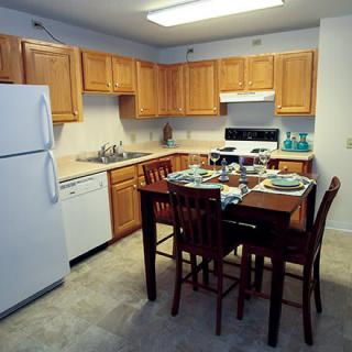 A cozy kitchen with wooden cabinets, a dining table set for four, and modern appliances including a refrigerator, stove, and dishwasher.