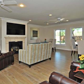 A spacious living room with a fireplace, television, and ample seating, featuring hardwood floors and large windows.