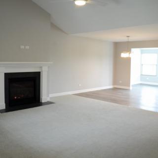 A spacious empty living room with a fireplace and adjacent dining area.