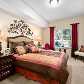 A cozy bedroom with elegant decor, featuring a plush bed, dark wood furniture, and red accents.