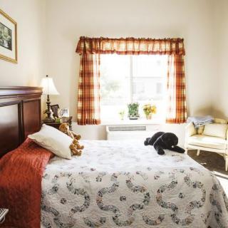 A cozy bedroom with natural light coming through a window, featuring a neatly made bed and warm decor.