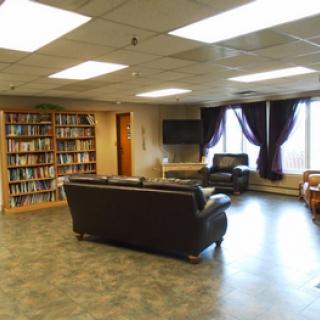 A cozy library lounge with bookshelves, seating area, and a television.