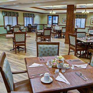 An empty dining room with neatly set tables and wooden flooring.