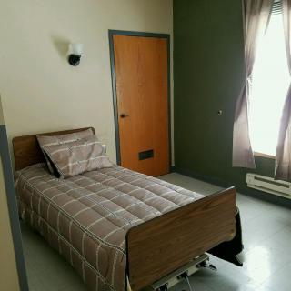 A minimalist bedroom featuring a single bed with plaid bedding, a window with curtains, and a wooden door.
