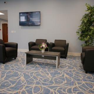A modern waiting area featuring comfortable black chairs, a coffee table, and a television.
