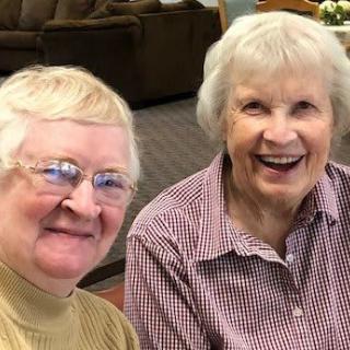 Two smiling elderly women enjoying time together indoors.