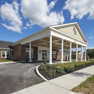 A wide entrance with a covered walkway leading to a brick building under a blue sky with clouds.