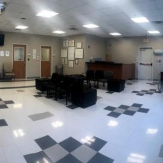 A spacious office waiting room with tiled flooring and black chairs.
