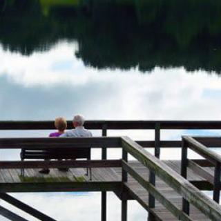 An elderly couple sitting on a bench overlooking a serene lake.