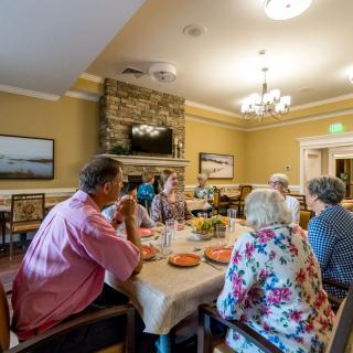 A group of people sitting around a dining table enjoying a meal and conversation in a warmly decorated room.