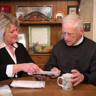 An elderly man and a woman reviewing documents together at a table.