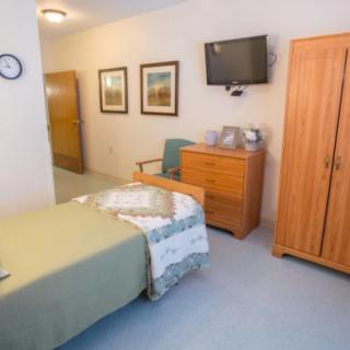 A neatly arranged single bedroom with a television, wardrobe, and bedside table.
